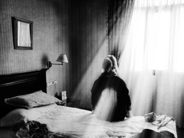 Quarto vazio em preto e branco, com a cama desfeita e a luz entrando pela cortina.