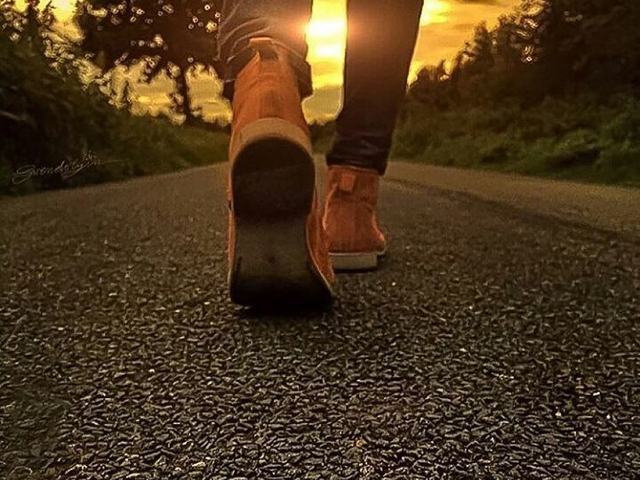 Pés caminhando por uma estrada de cascalho em direção ao sol baixo.