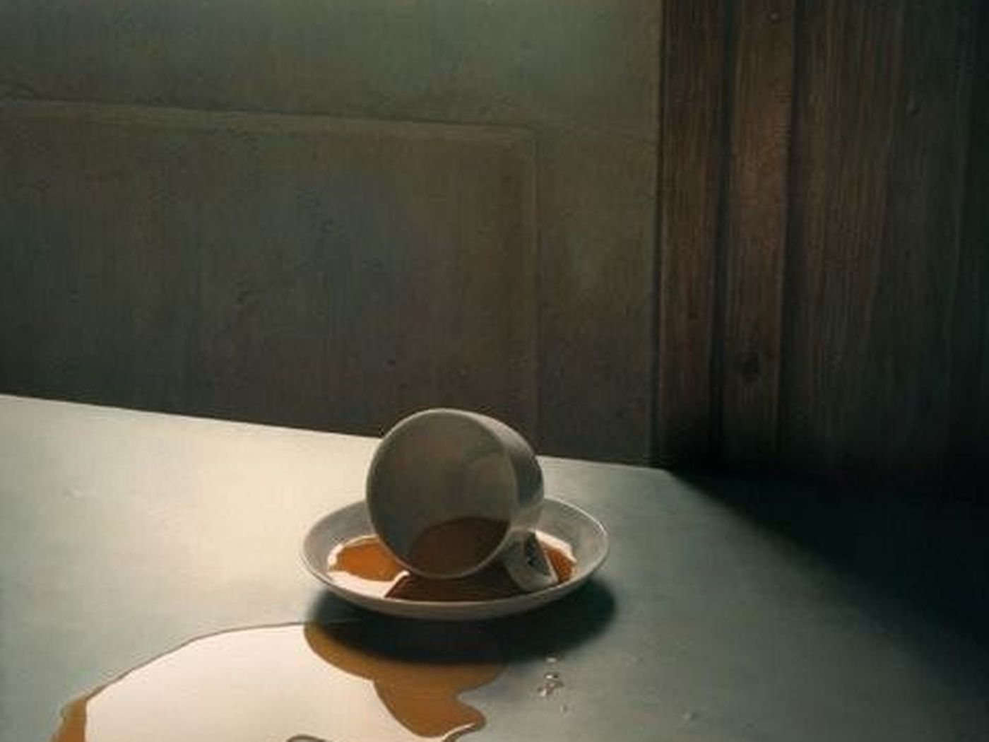 Xícara de café virada sobre uma mesa, com a bebida derramada, à luz da janela.