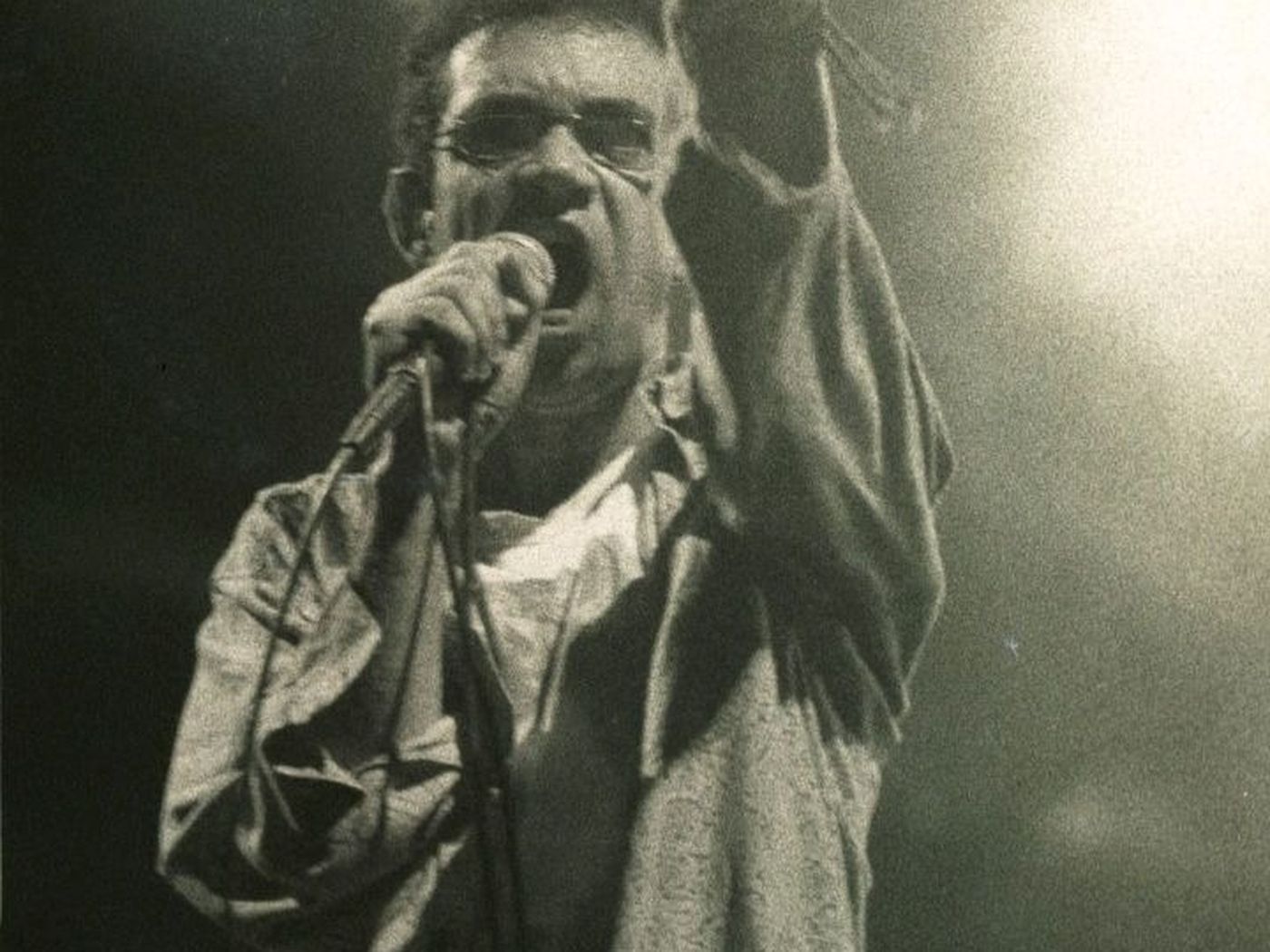 Fotografia em preto e branco de Renato Russo cantando ao microfone.
