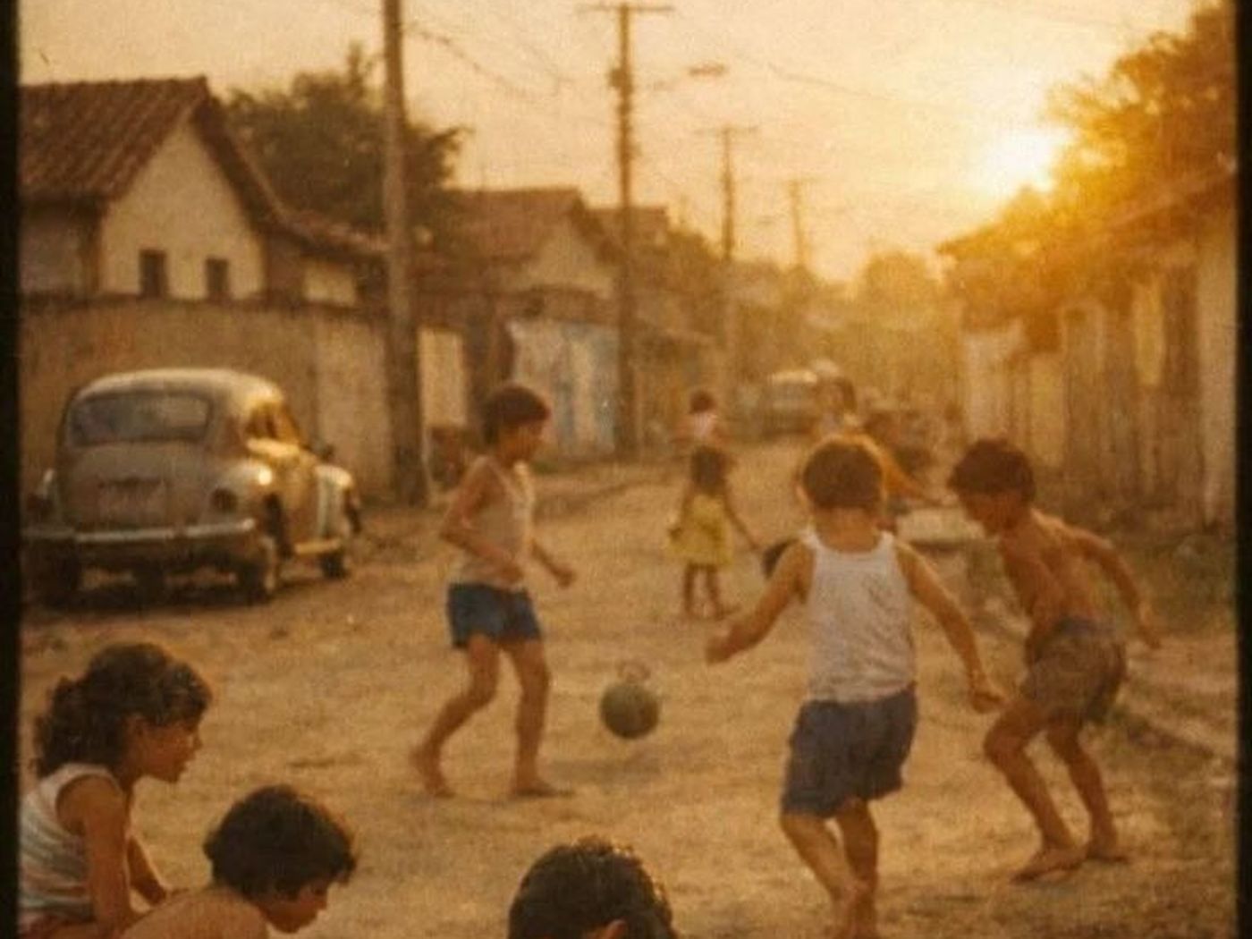Crianças brincando descalças na rua de terra de um bairro, ao entardecer.
